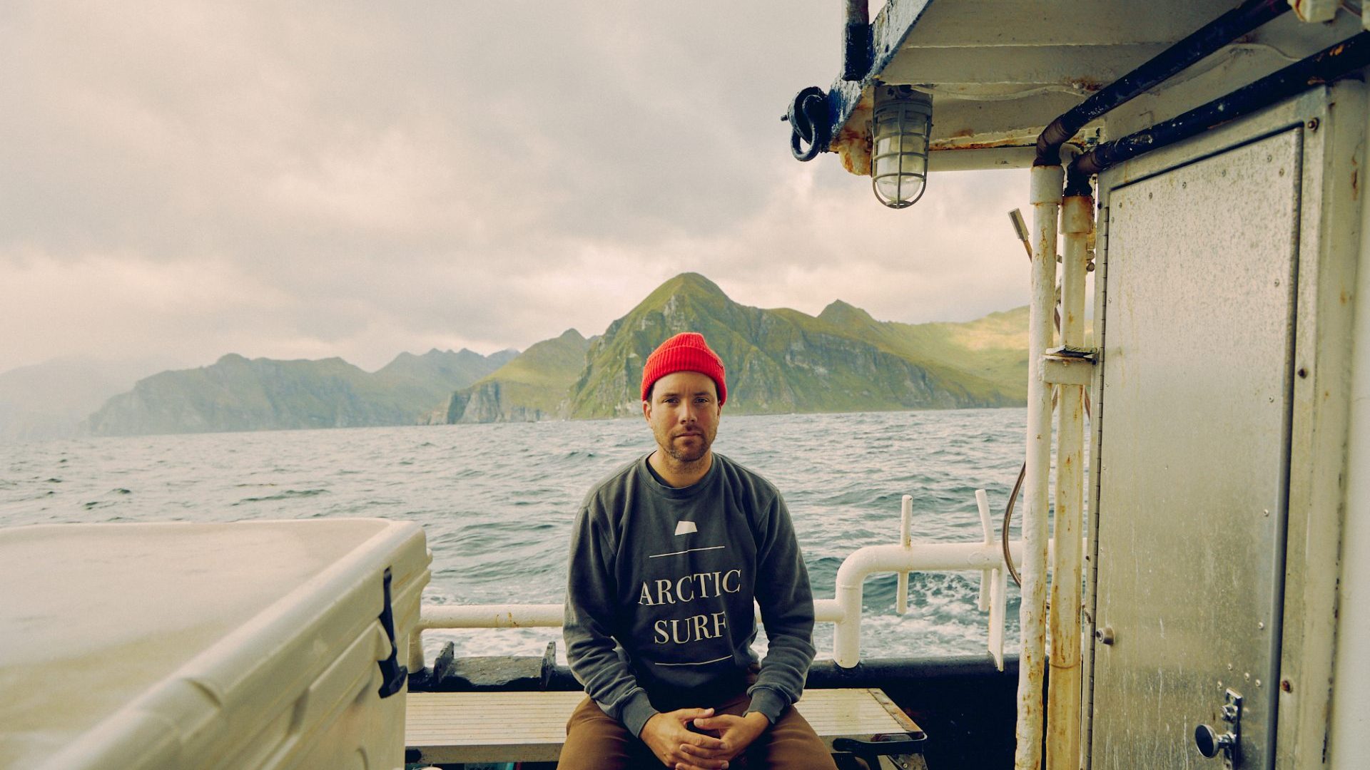 Man in red beanie sits on deck of boat and smiles
