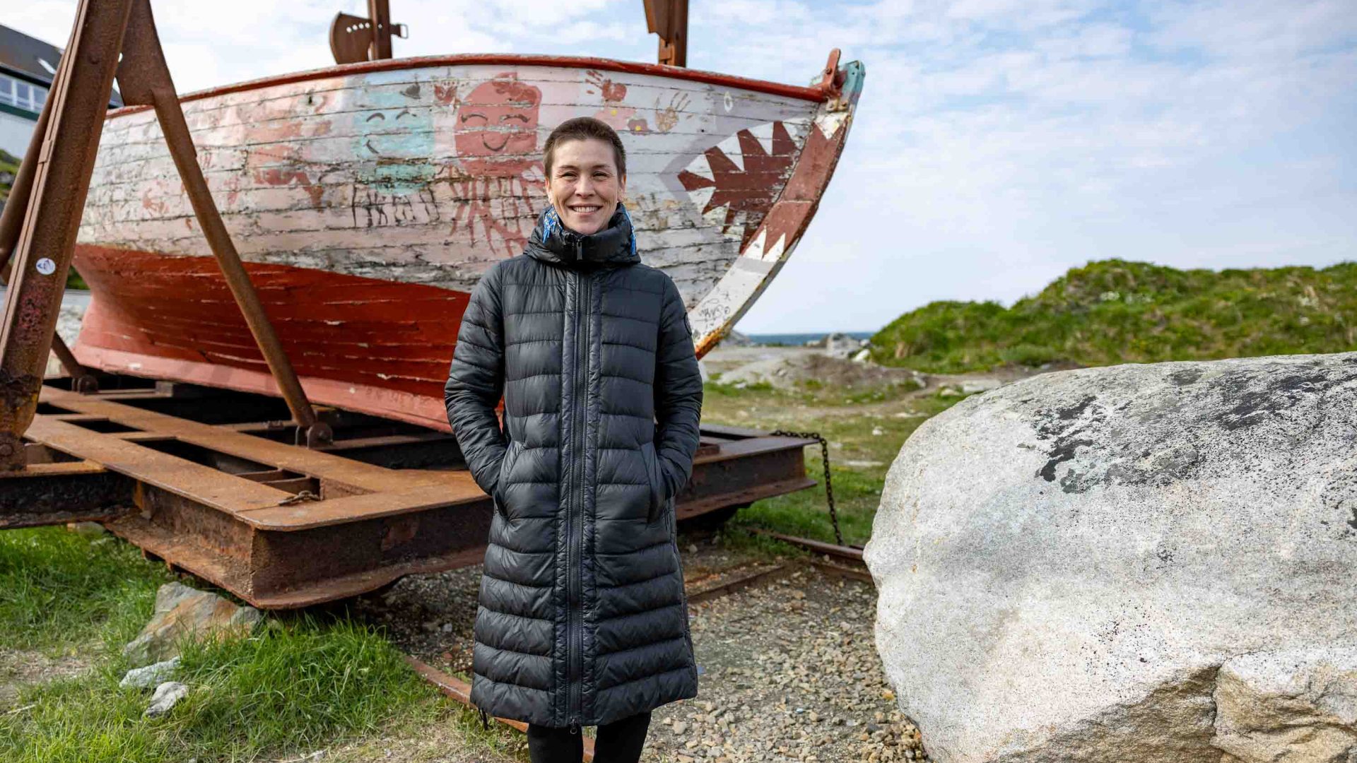 A woman stands in front of a painted boat.