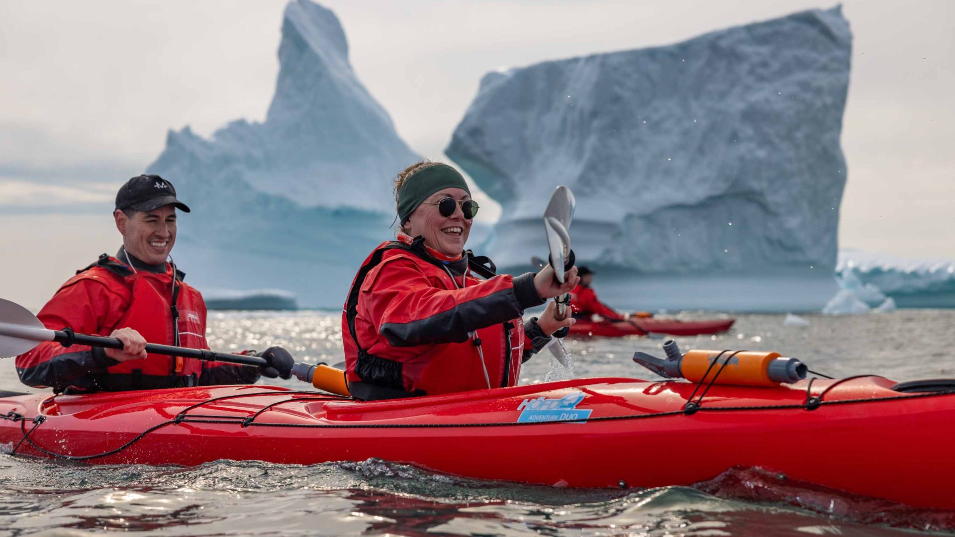 Two people kayak past icebergs.