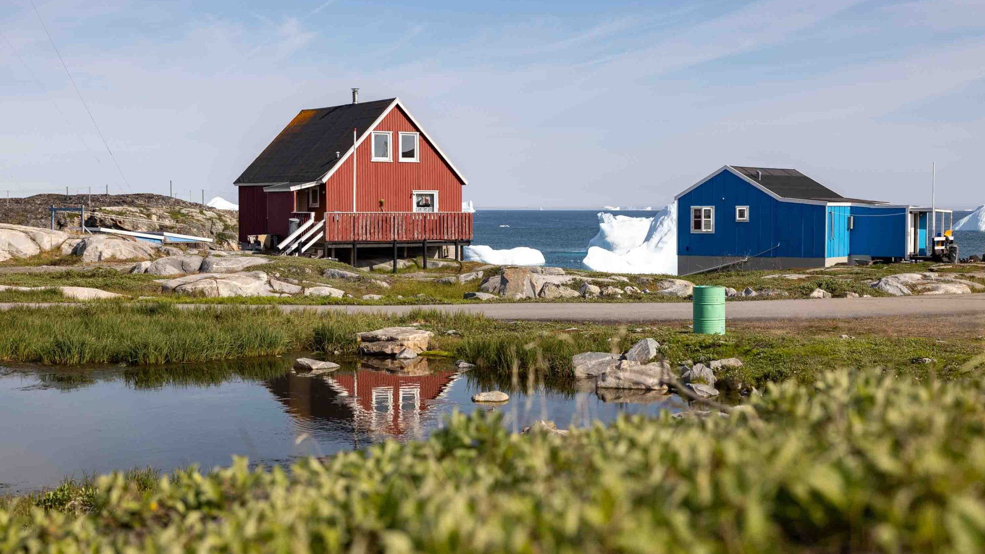 A red and blue house are reflected in a pond.