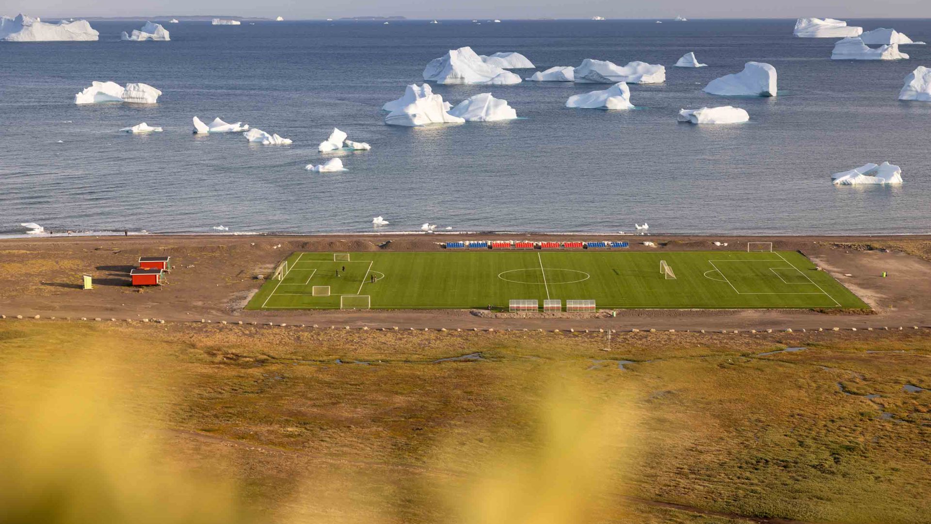 A sportsfield alongside water with glaciers.