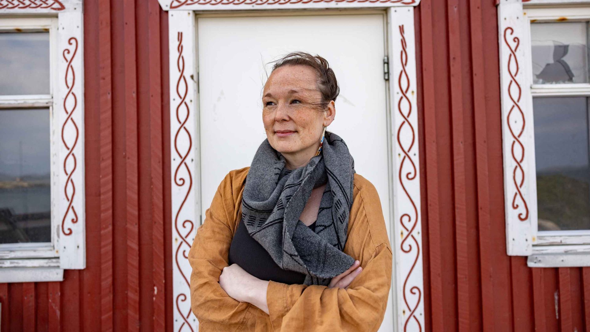 A woman stands in front of the door of a red building.