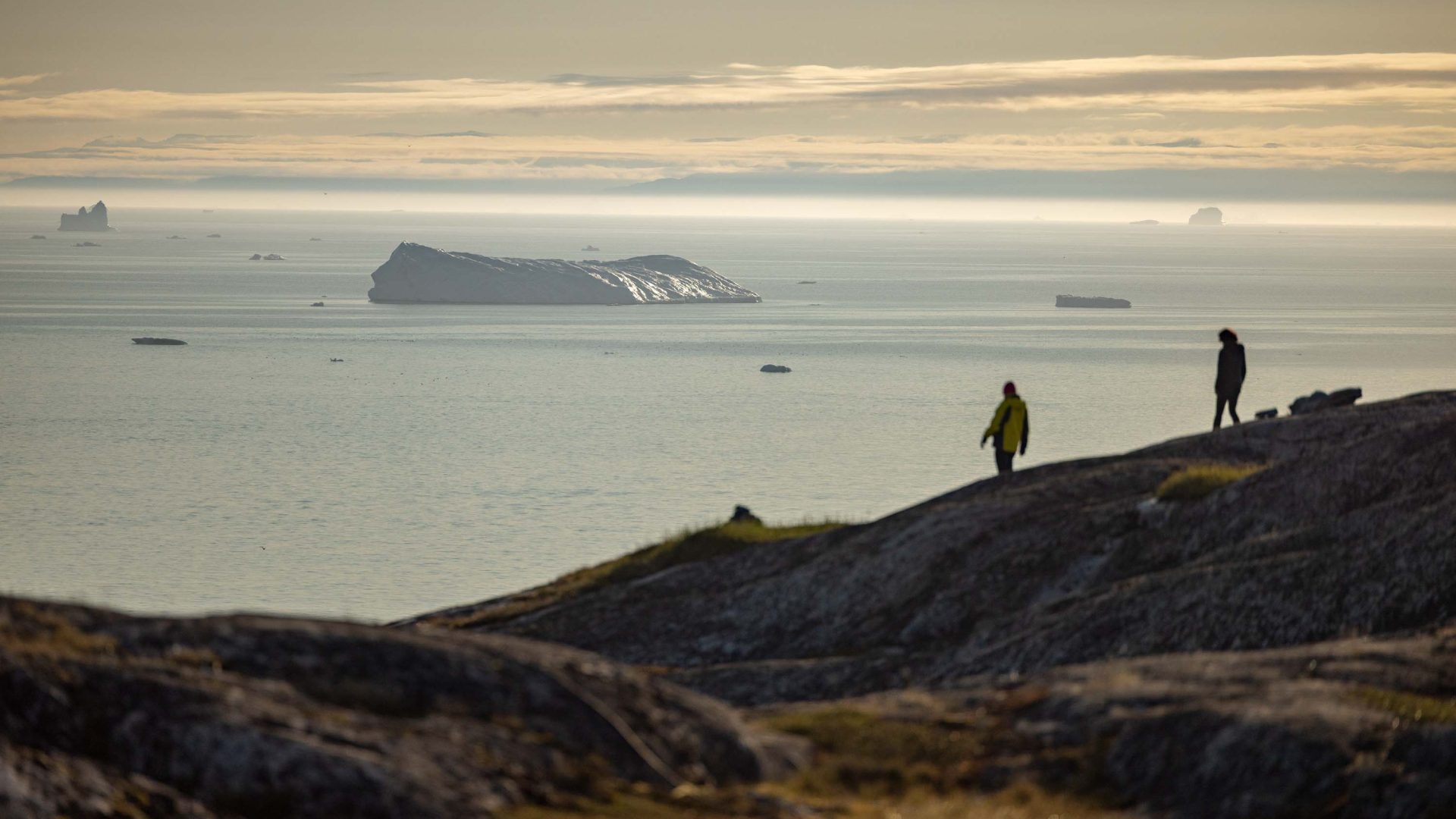 In low light, a person looks out from a cliff over the sea.