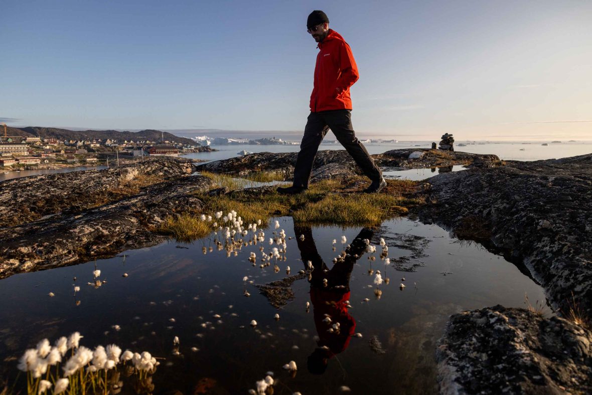A man in red walks past a puddle.