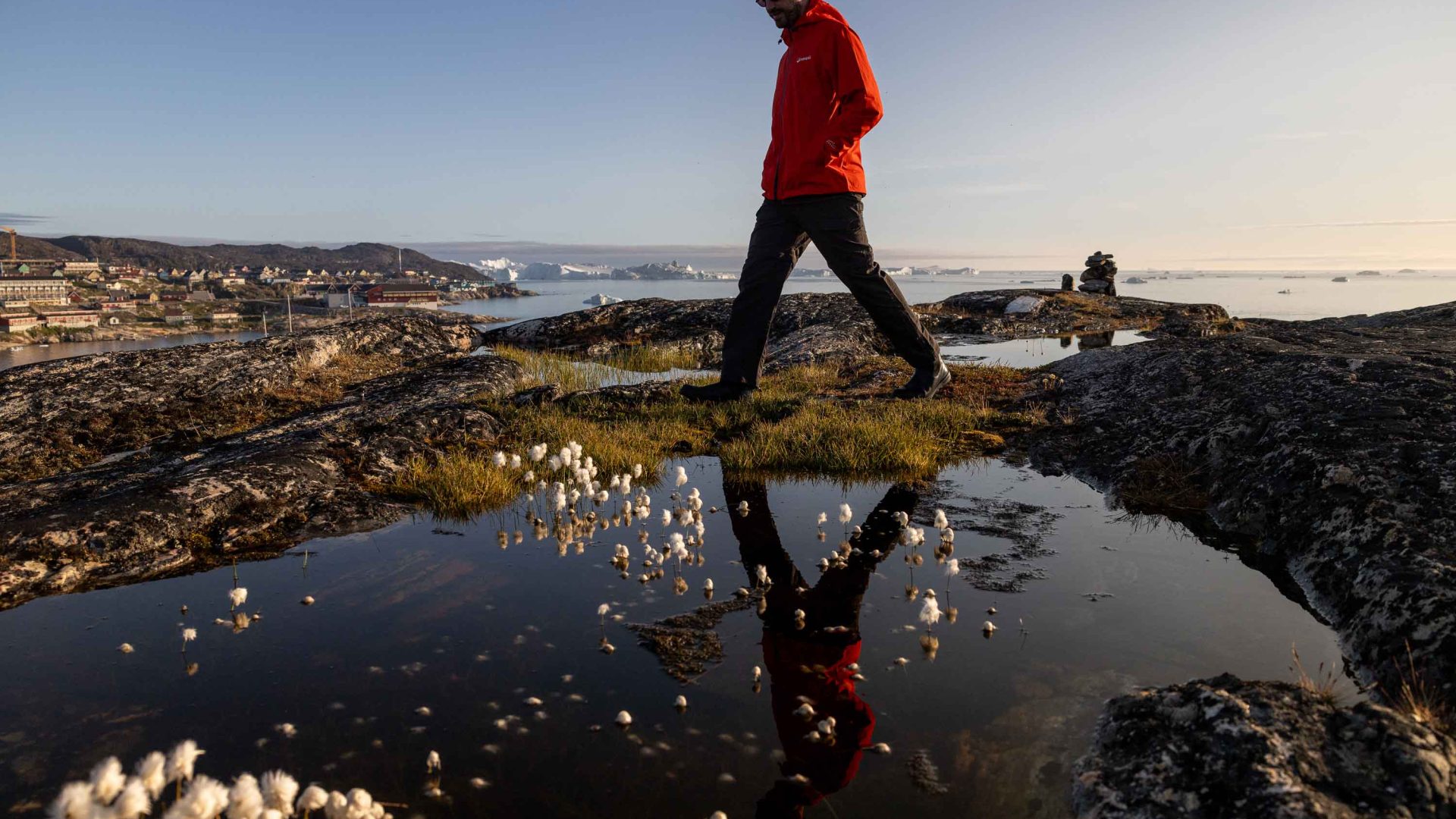 A man in red walks past a puddle.