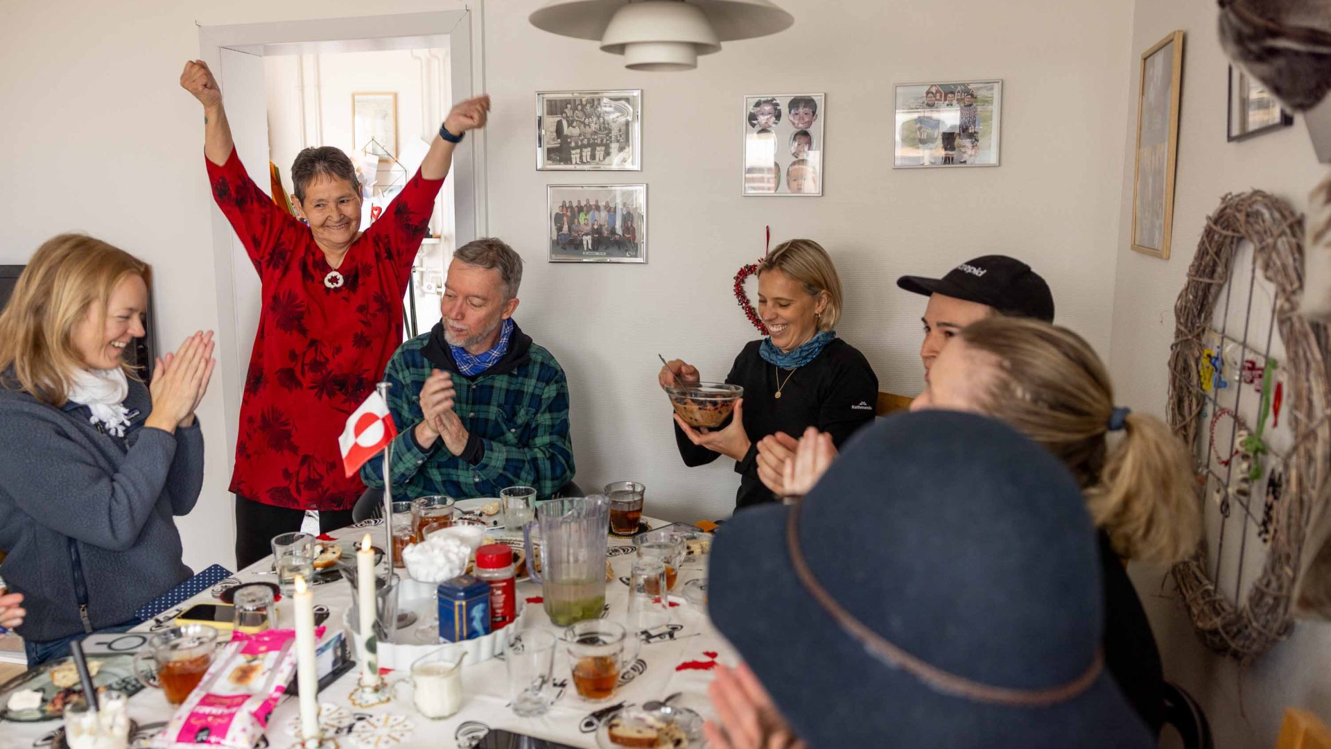 People enjoy a meal at a table. One woman smiles and raises her arms.