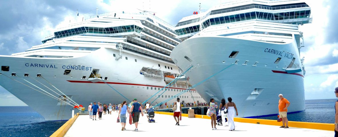 People walk toward two big cruise ships.