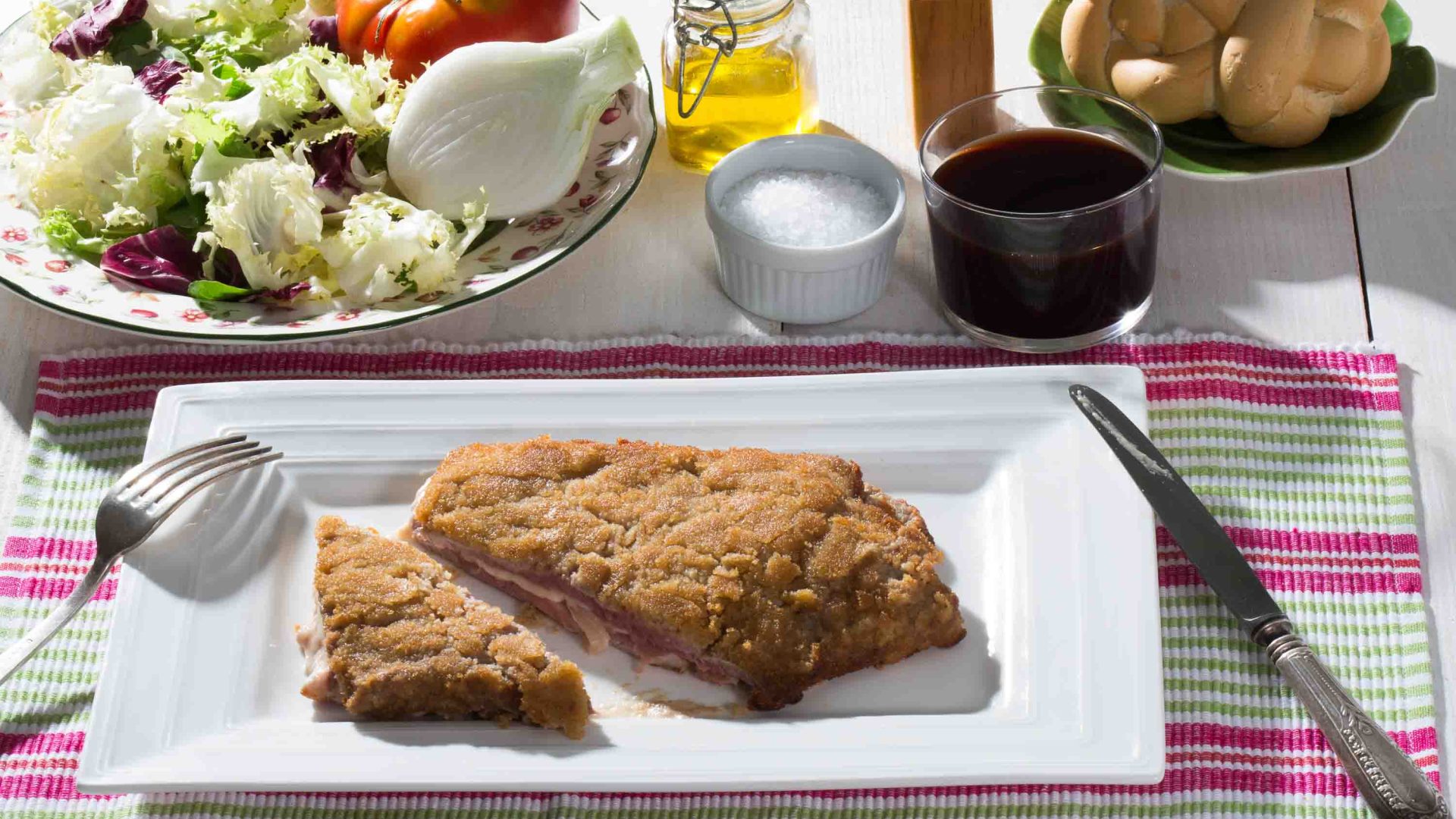 A dish of beef in breadcrumbs on a plate alongside salad, oil and salt.
