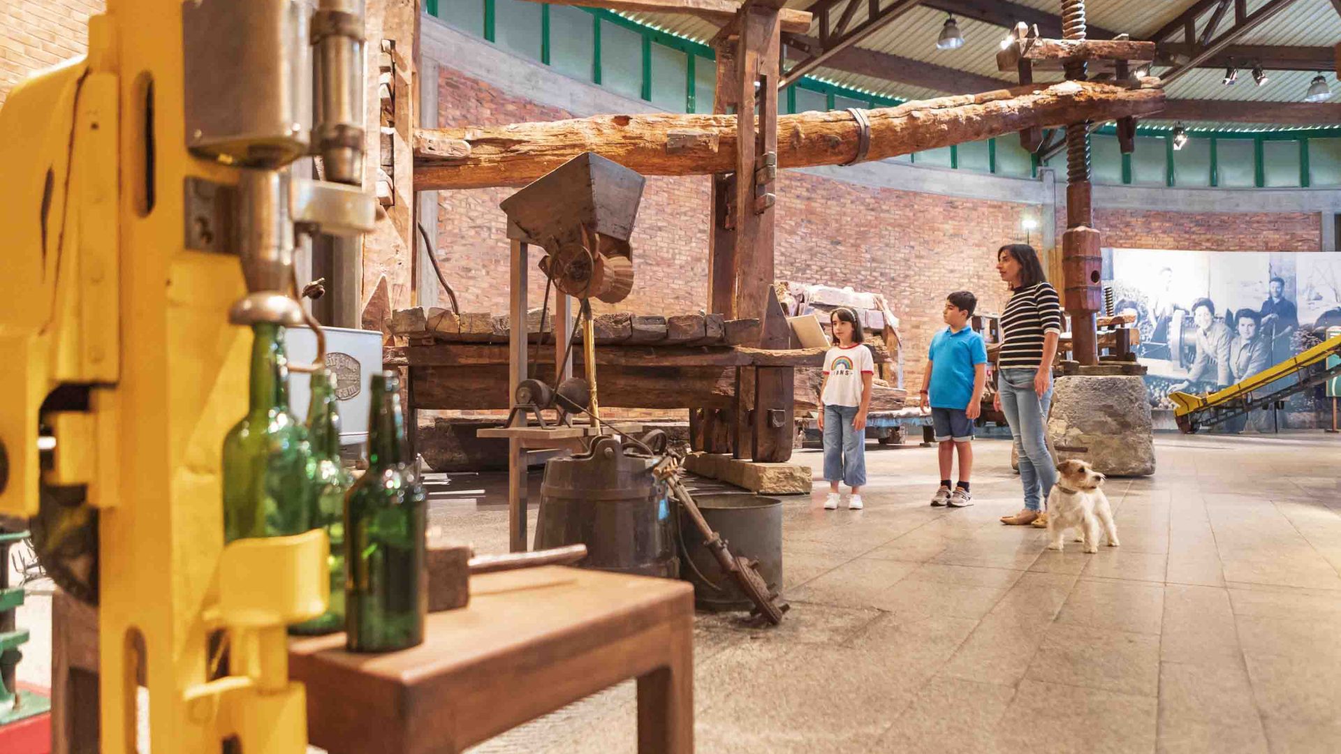 A woman and children look at old cider making equipment in a museum.