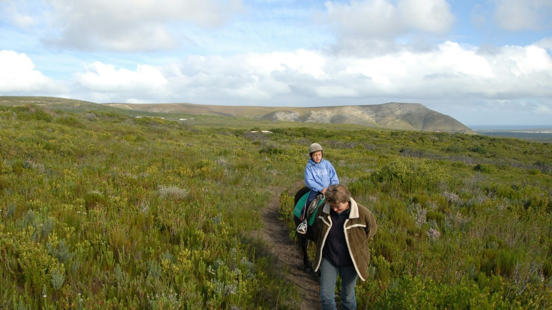 One person horseback-riding and one hiking through the fields