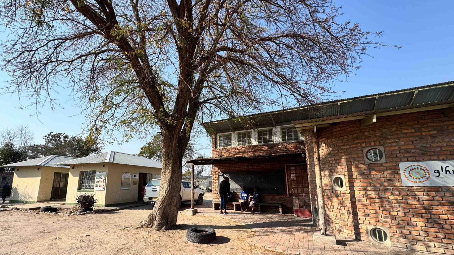 A small brick building and another smaller white building alongside a tree.