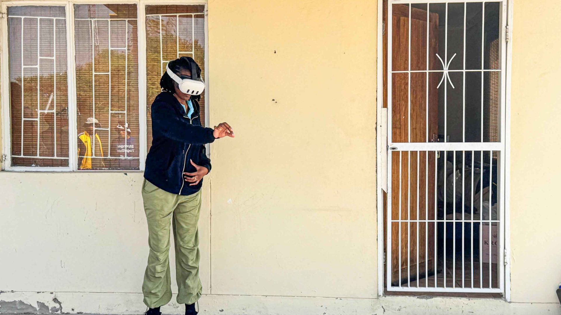 A woman stands next to a building in a VR headset.