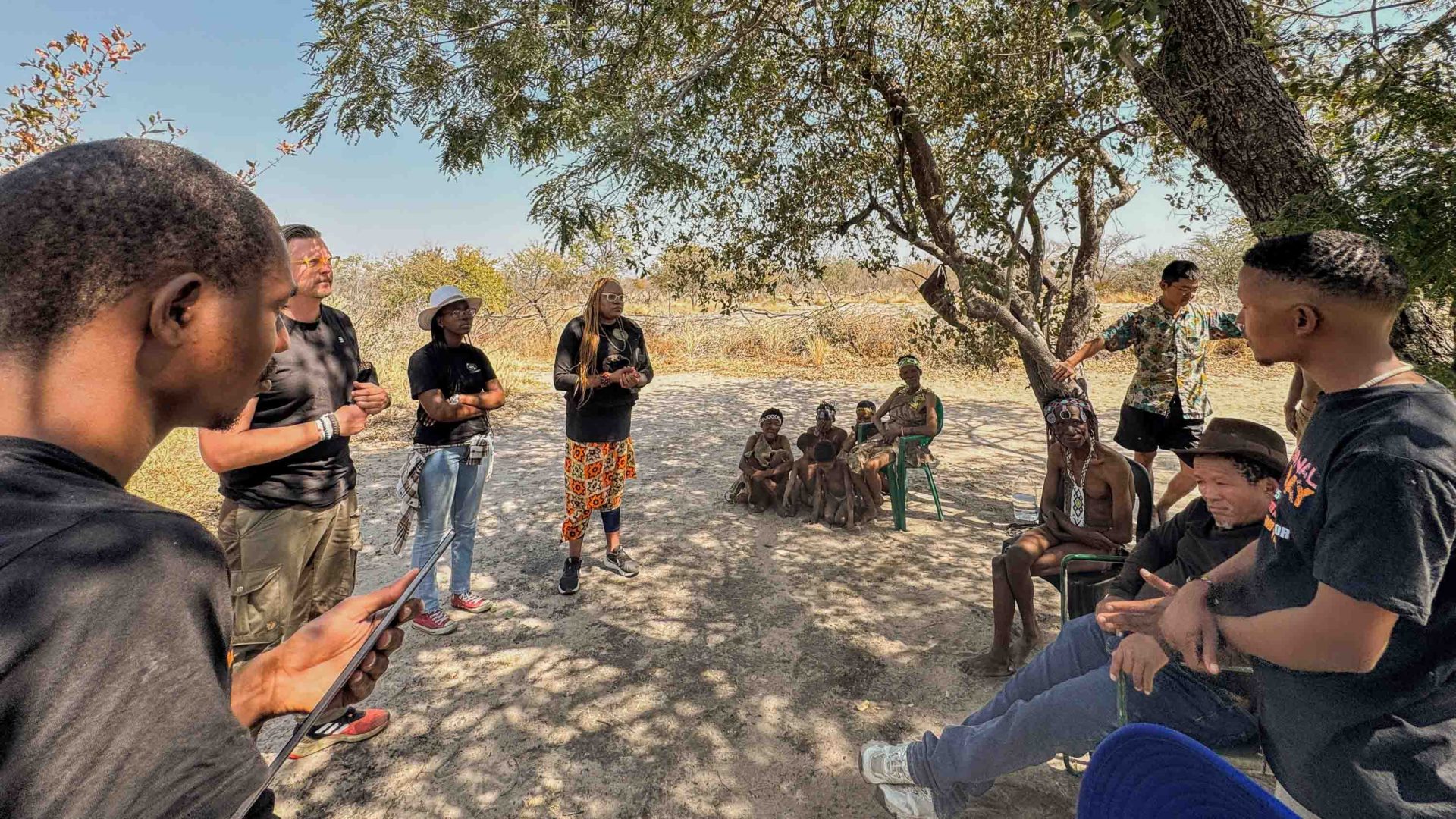 A group of people meet under a tree in an otherwise fairly barren environment.
