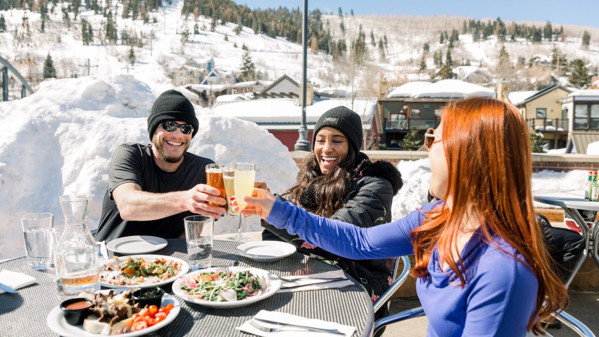 Three people 'cheers' drinks while eating at a ski resort