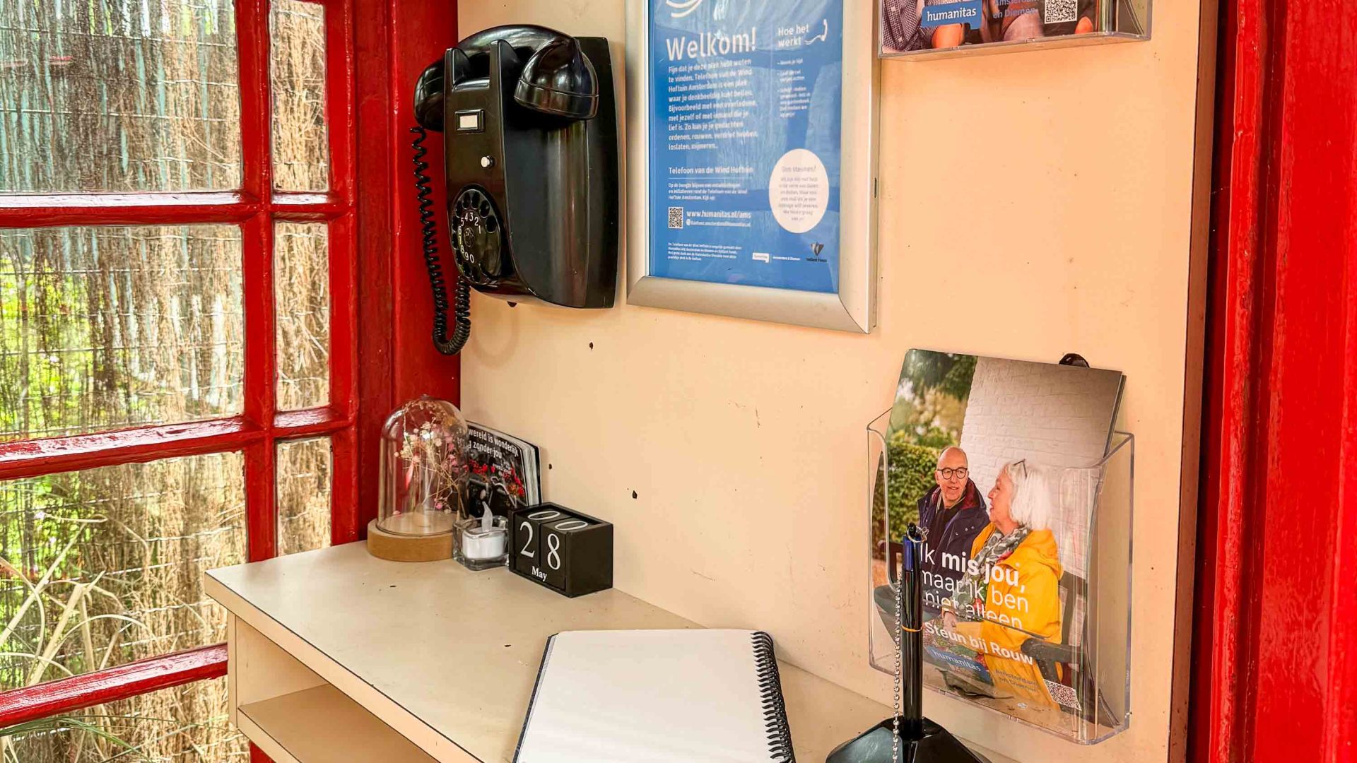 A black phone inside a red phone booth with posters on the wall.