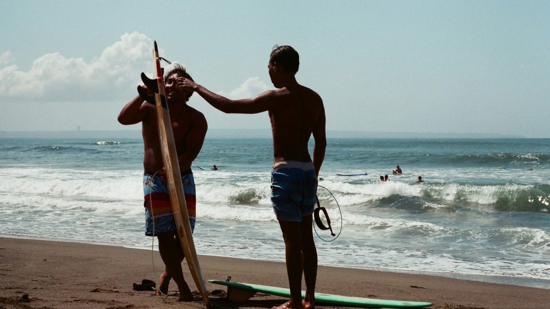 Two men stand on beach with surfboard