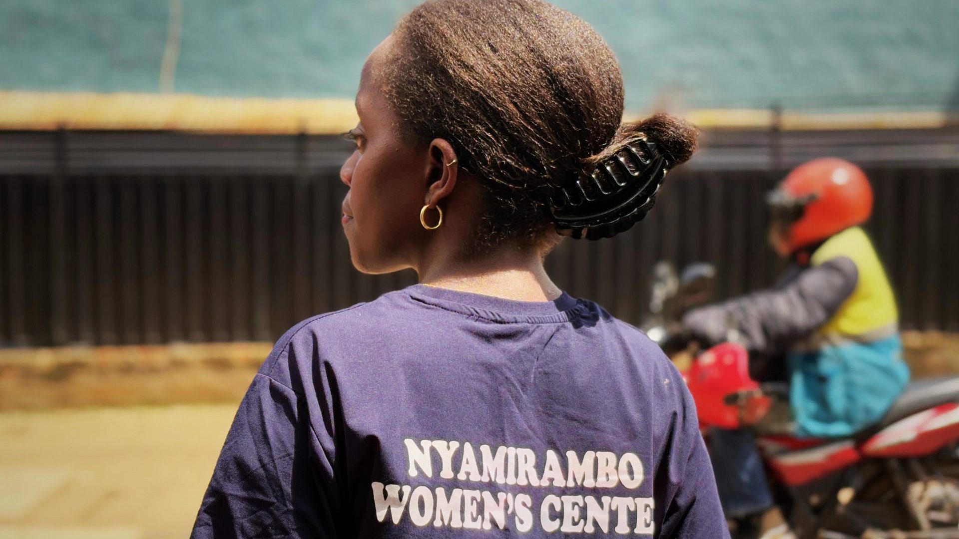 A woman wearing a blue shirt reading 'Nyamirambo Women's Center'.