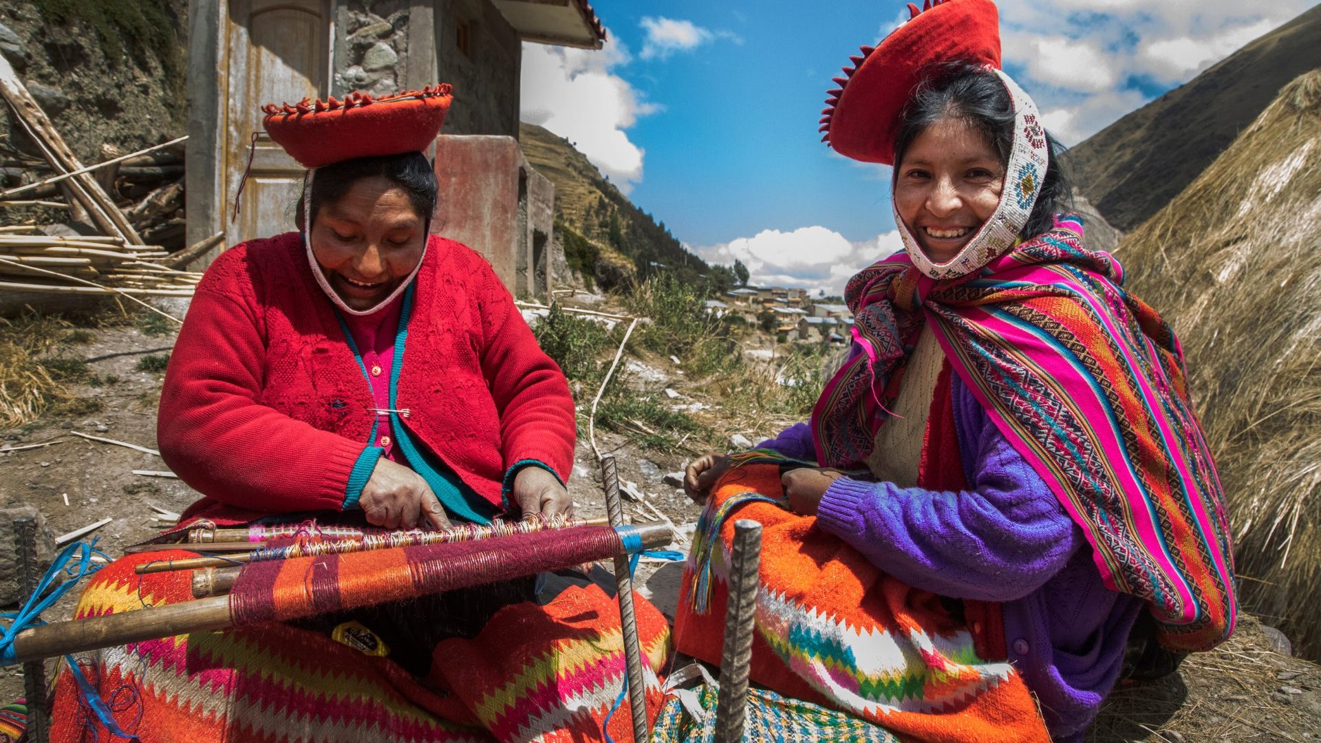 Two women weaving and smiling under blue skies.