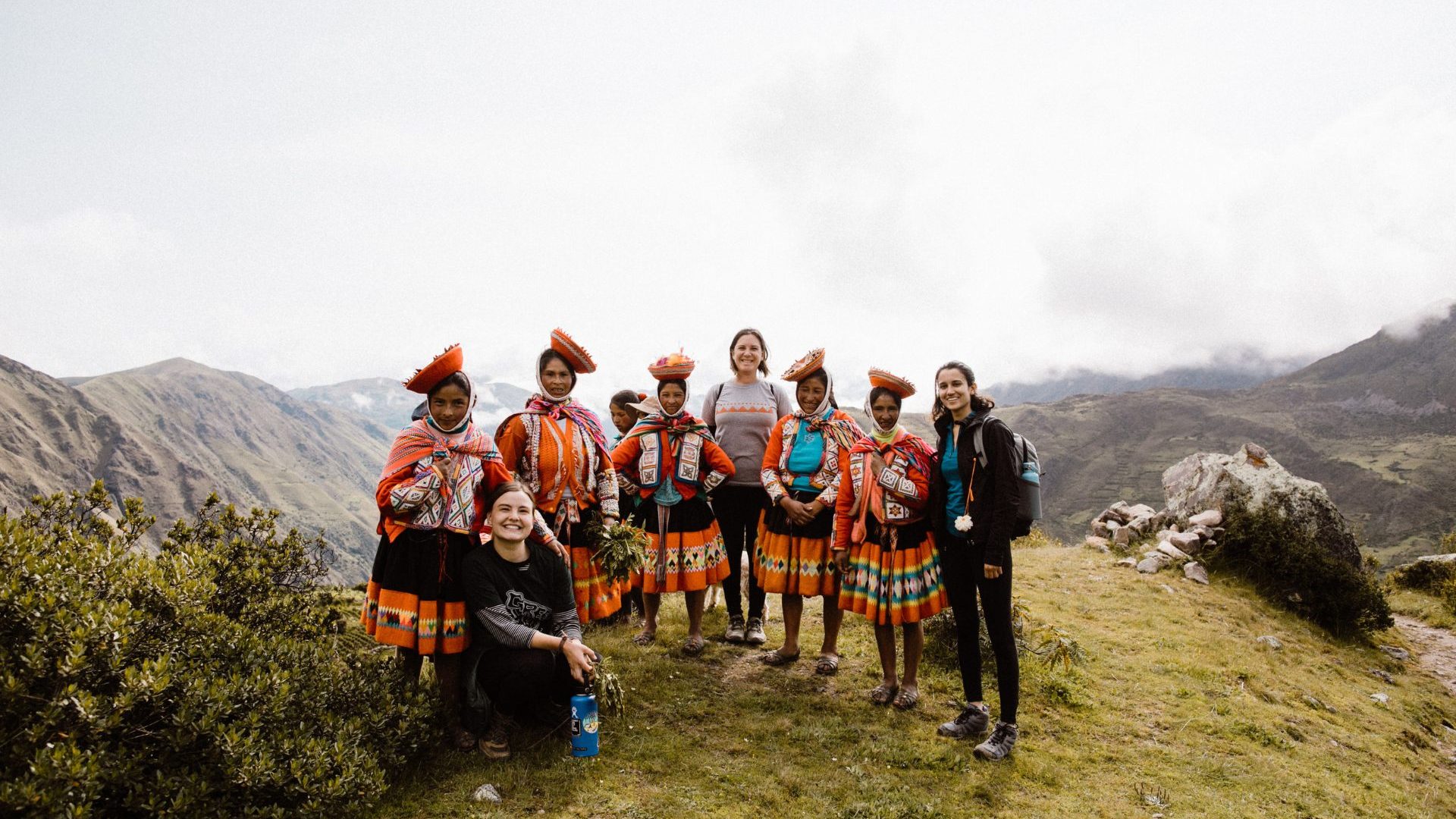 A group of local women and travelers pose for a group photo on mountain top.