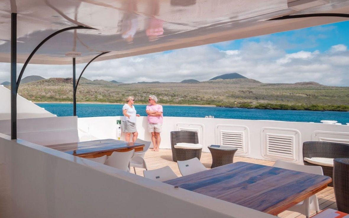Two people chat on a boat as it sails past islands