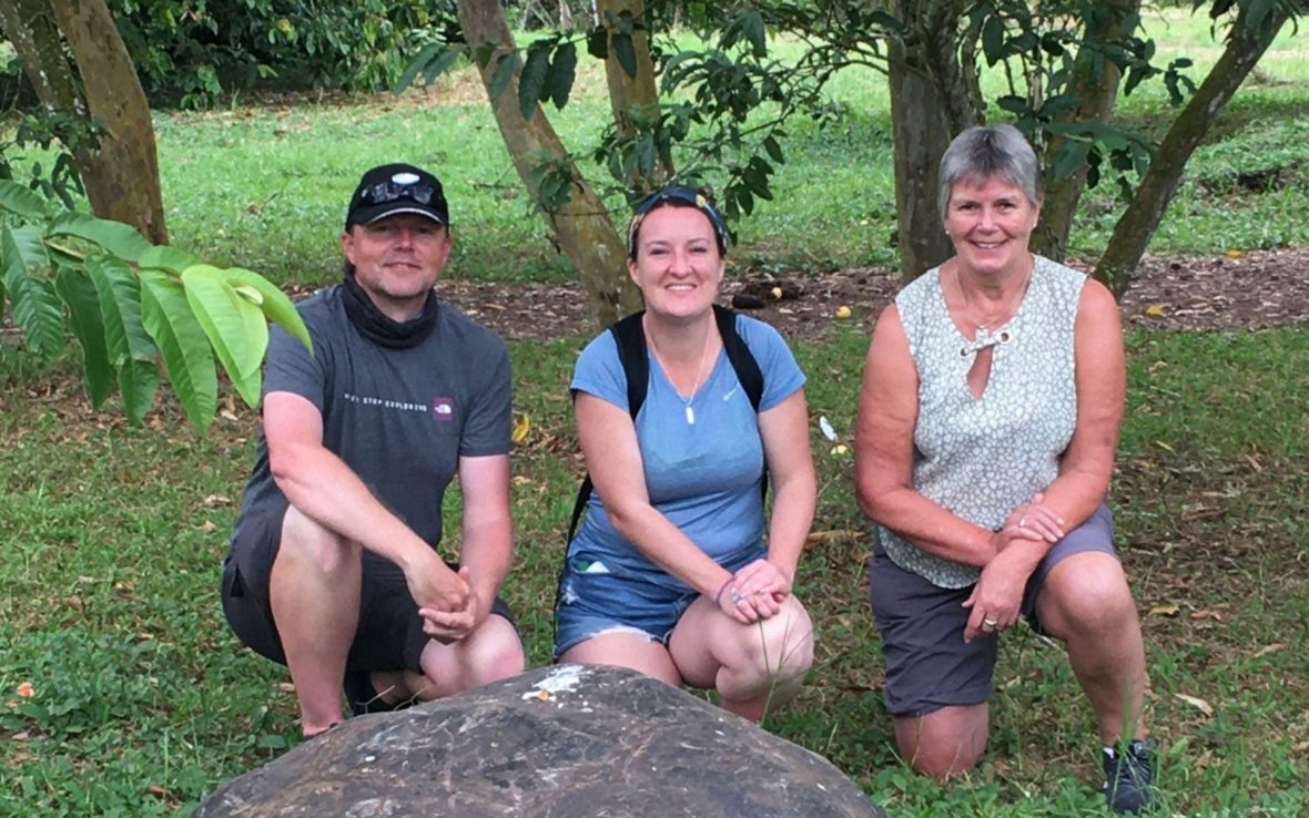A man and two women crouch against a green parkland background as they pose for a photo