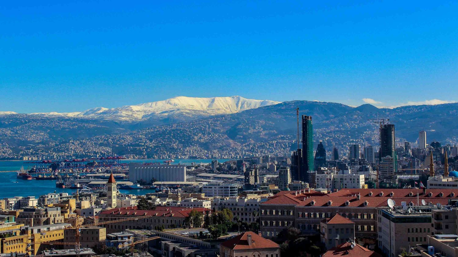 A city and lake in the foreground and snowy mountains in the background.