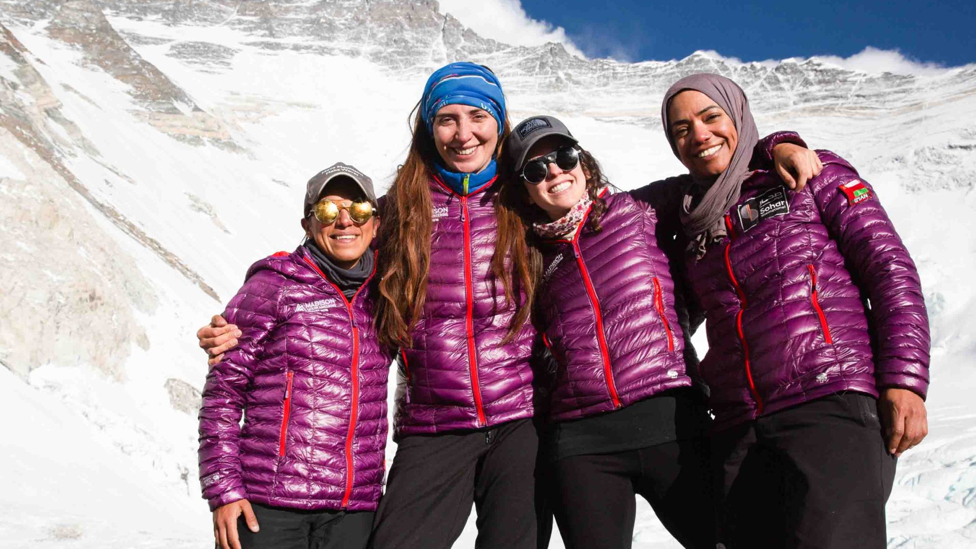 Four women smile as they stand in front of a snowy mountain.