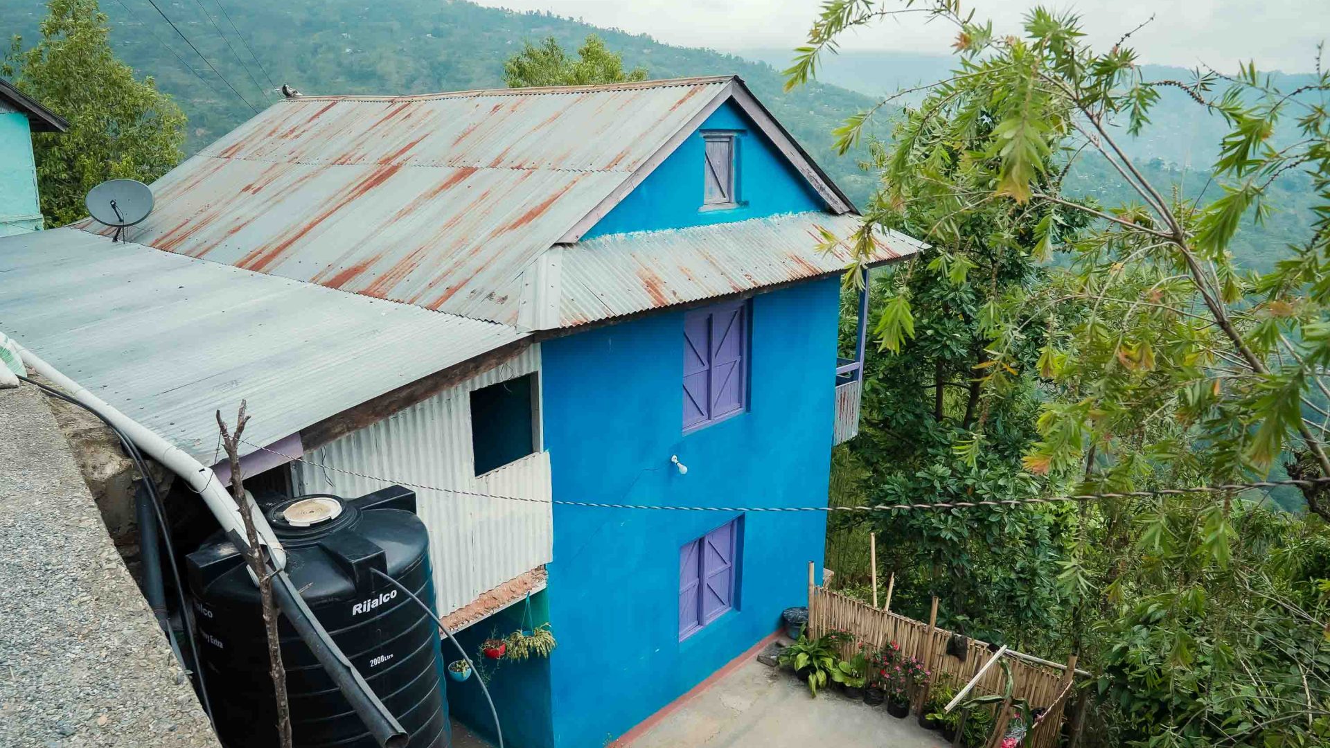 A blue house on the edge of a green valley.