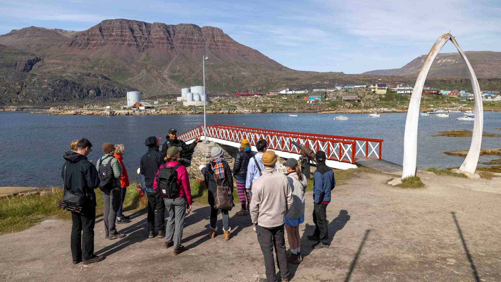 A tour group stands next to a red and white bridge with a whale bone arch nearby.