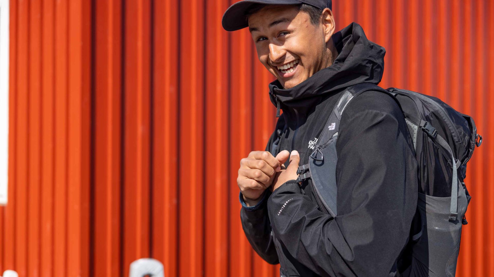 A man in a black jacket and black hat walks past a red structure.