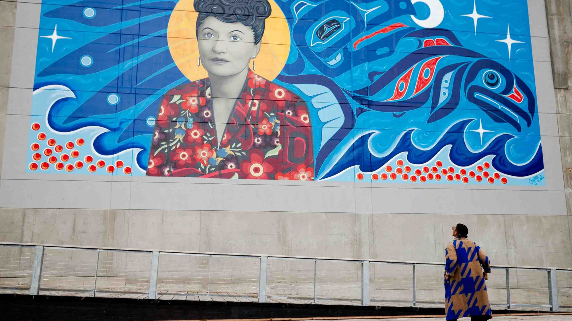 A woman looks up at a mural of a woman.