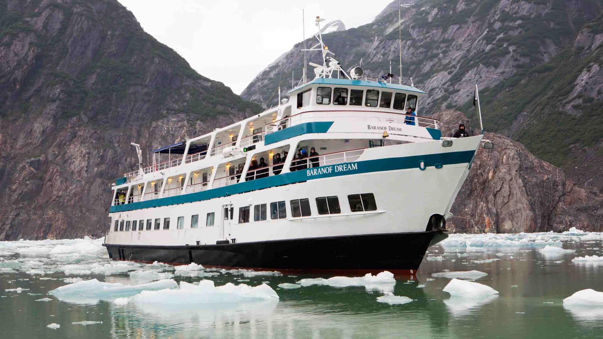 A white and blue cruise boat passes through ice.
