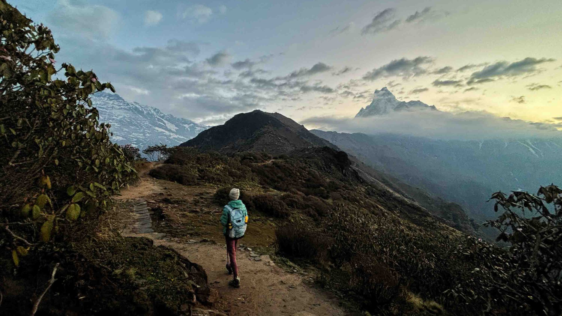 A person walks along a trail with mountains off to the right.