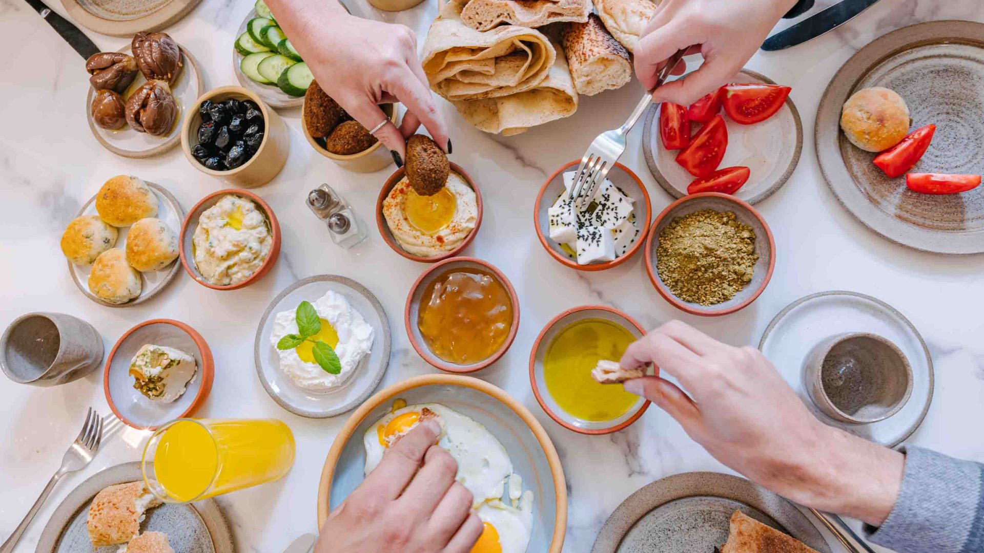 Shot from above, hands reach out for an assortment of Palestinian foods including bread, falafel, and dips.