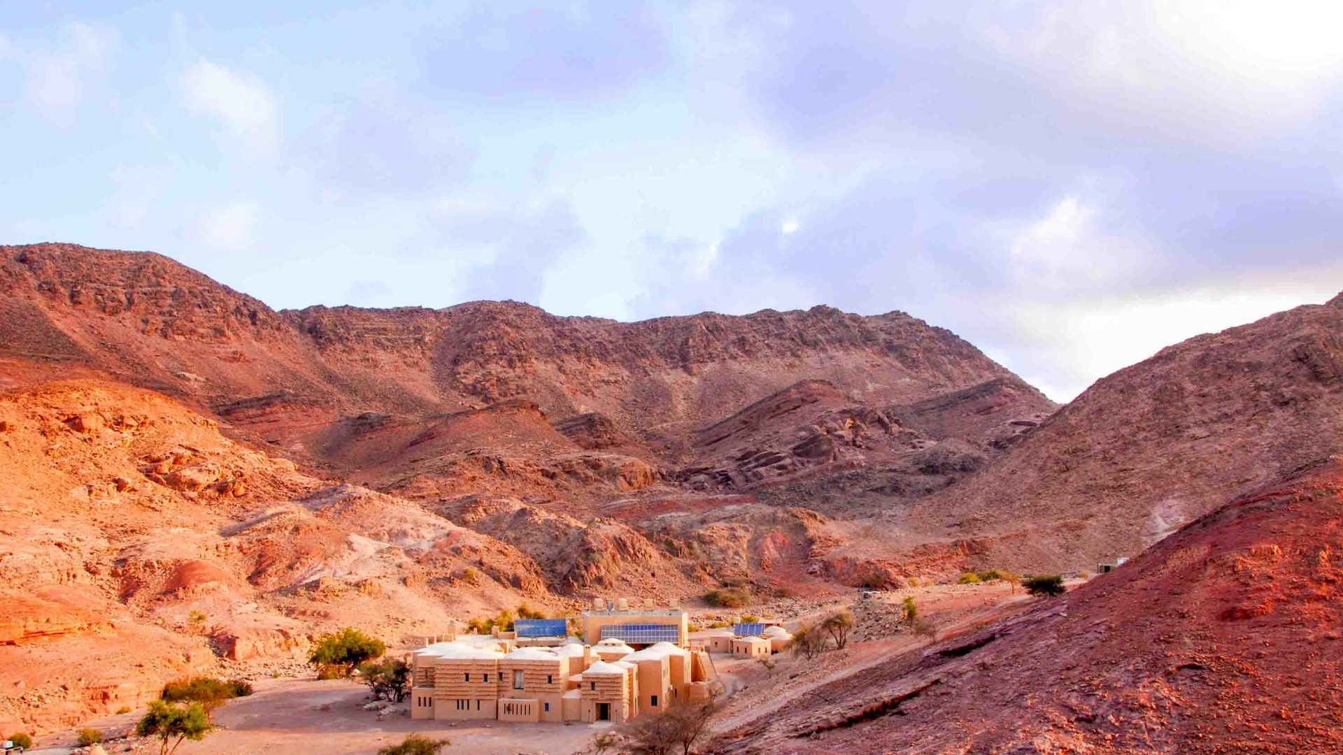 A lodge sits below barren hills that have a read earth colour.