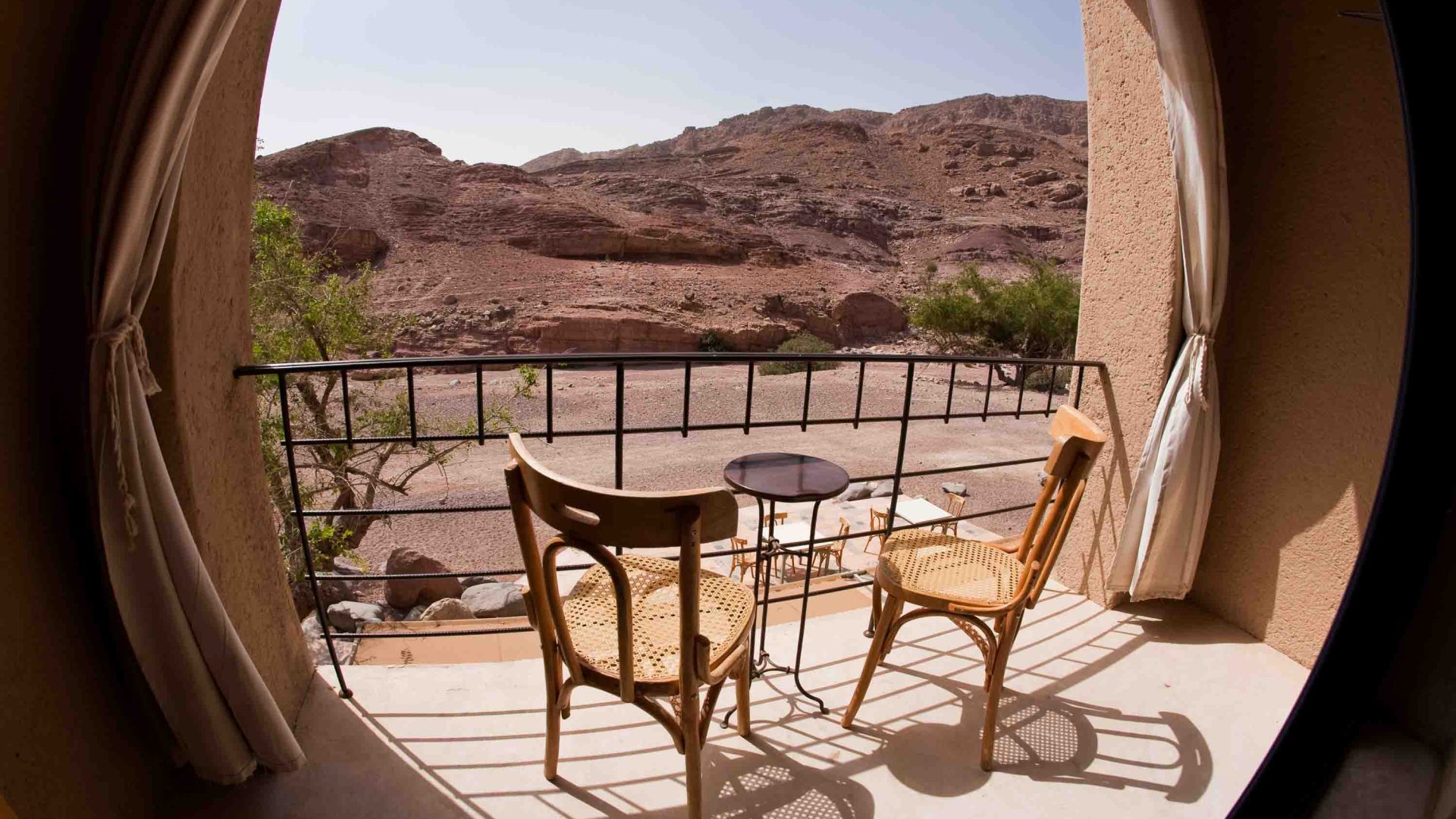 Two chairs and a table on a balcony framed by an arch. the view is of hills.