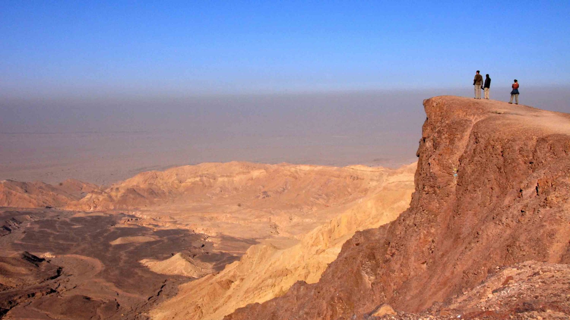 Three people look out at vast read earth hills in the desert.