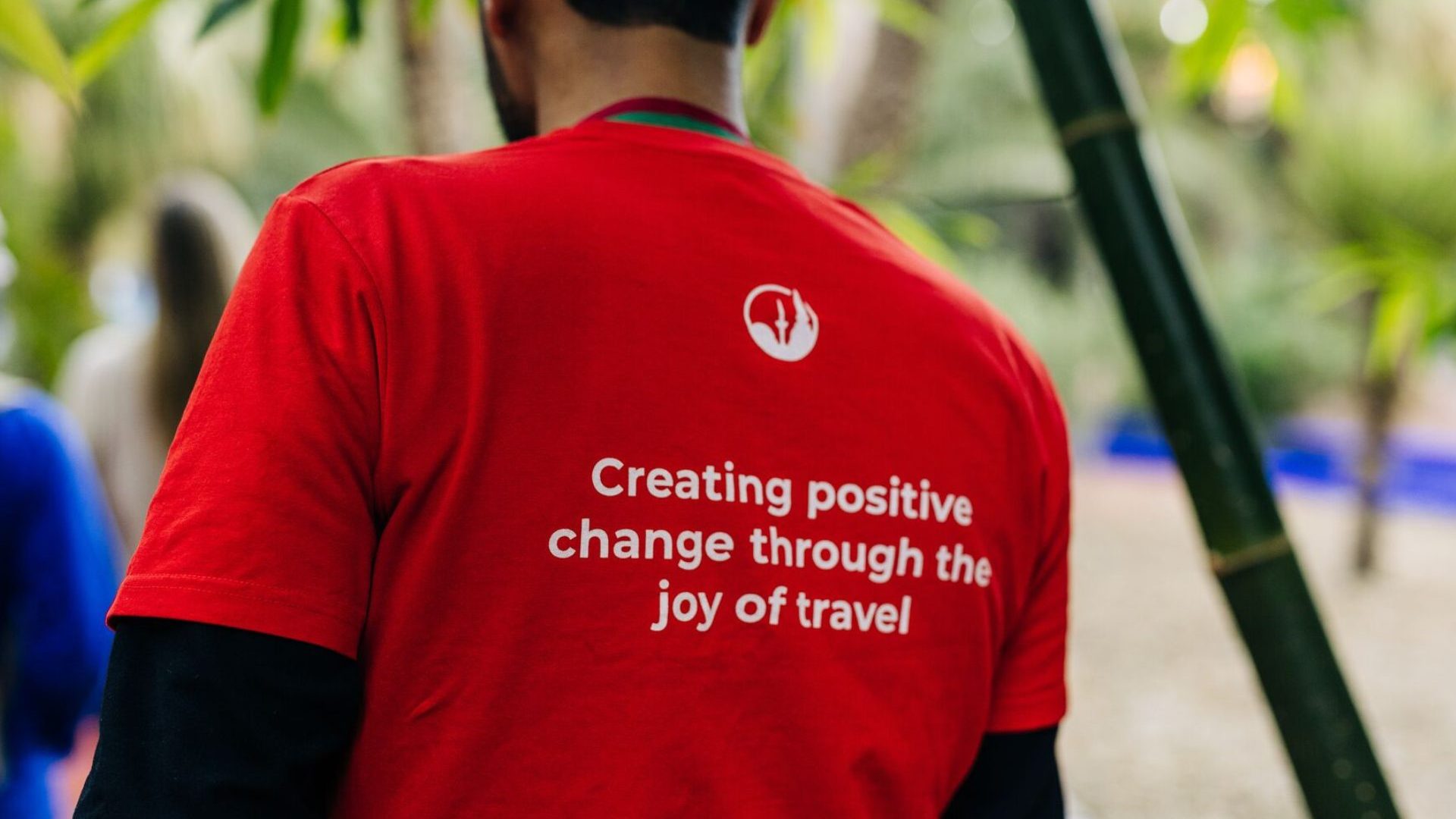 A man wearing a red shirt which reads: "Creating positive change through the joy of travel."
