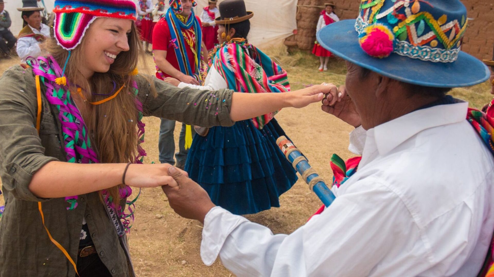 Woman dances with local man in Peru, both wear colorful traditional hats