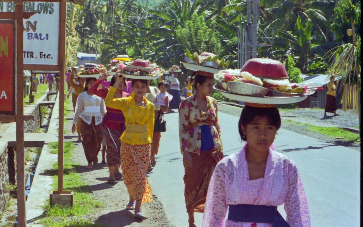 Balinese women in colorful traditional dress carry offerings on their heads