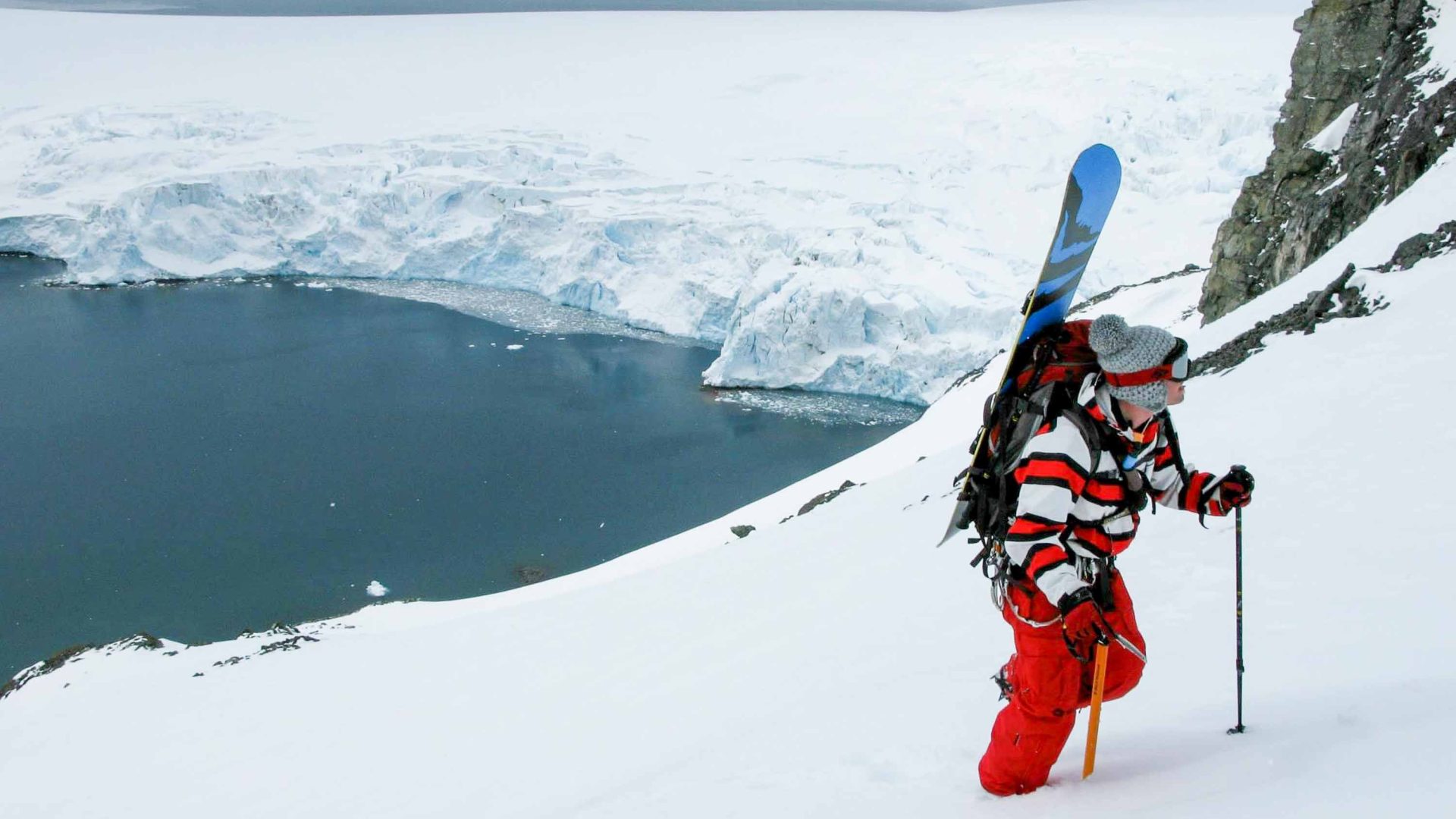 A man in a red snow suit walks up a mountain.