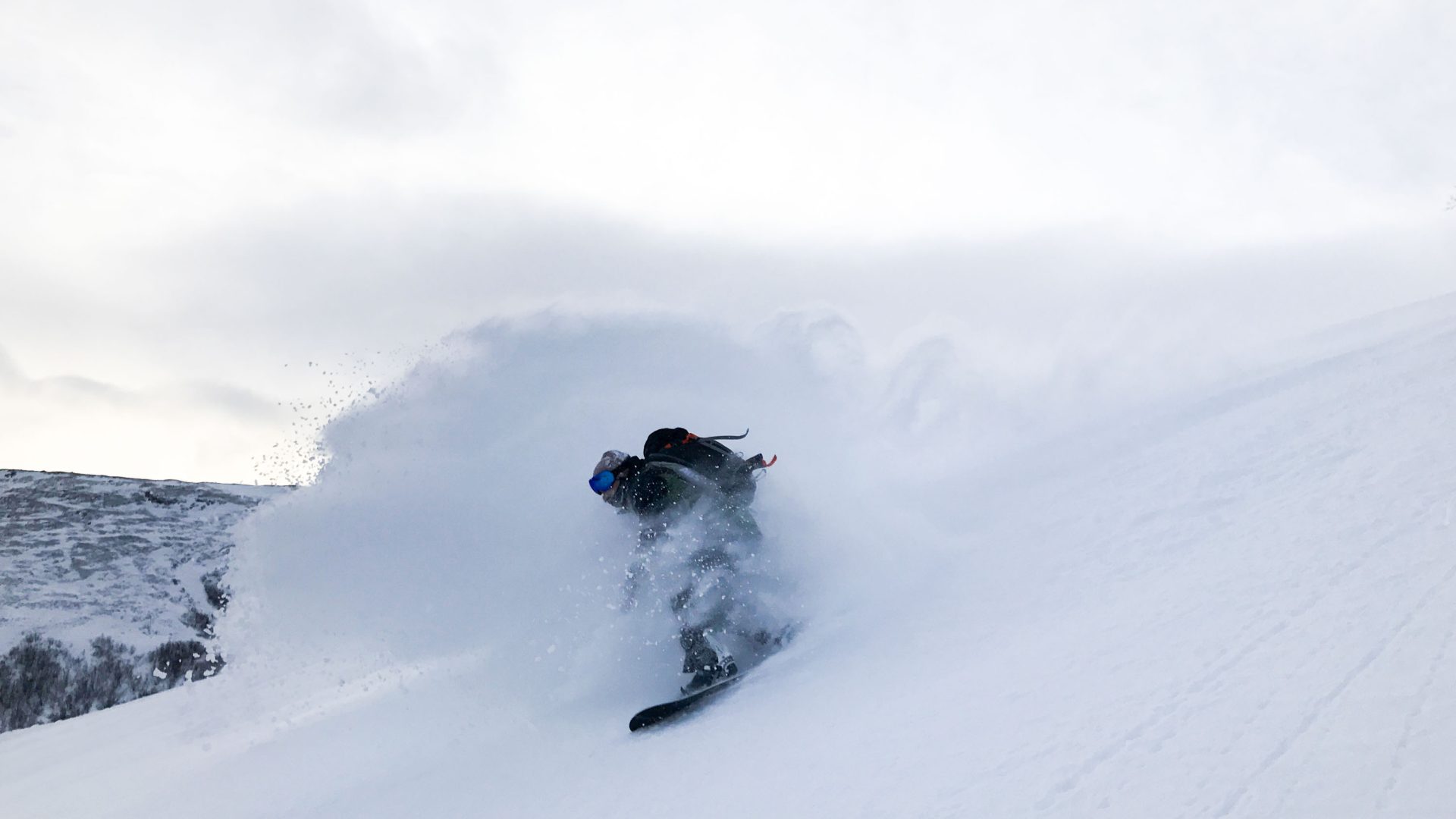 A snowboarder creates a spray of snow that covers him while riding.