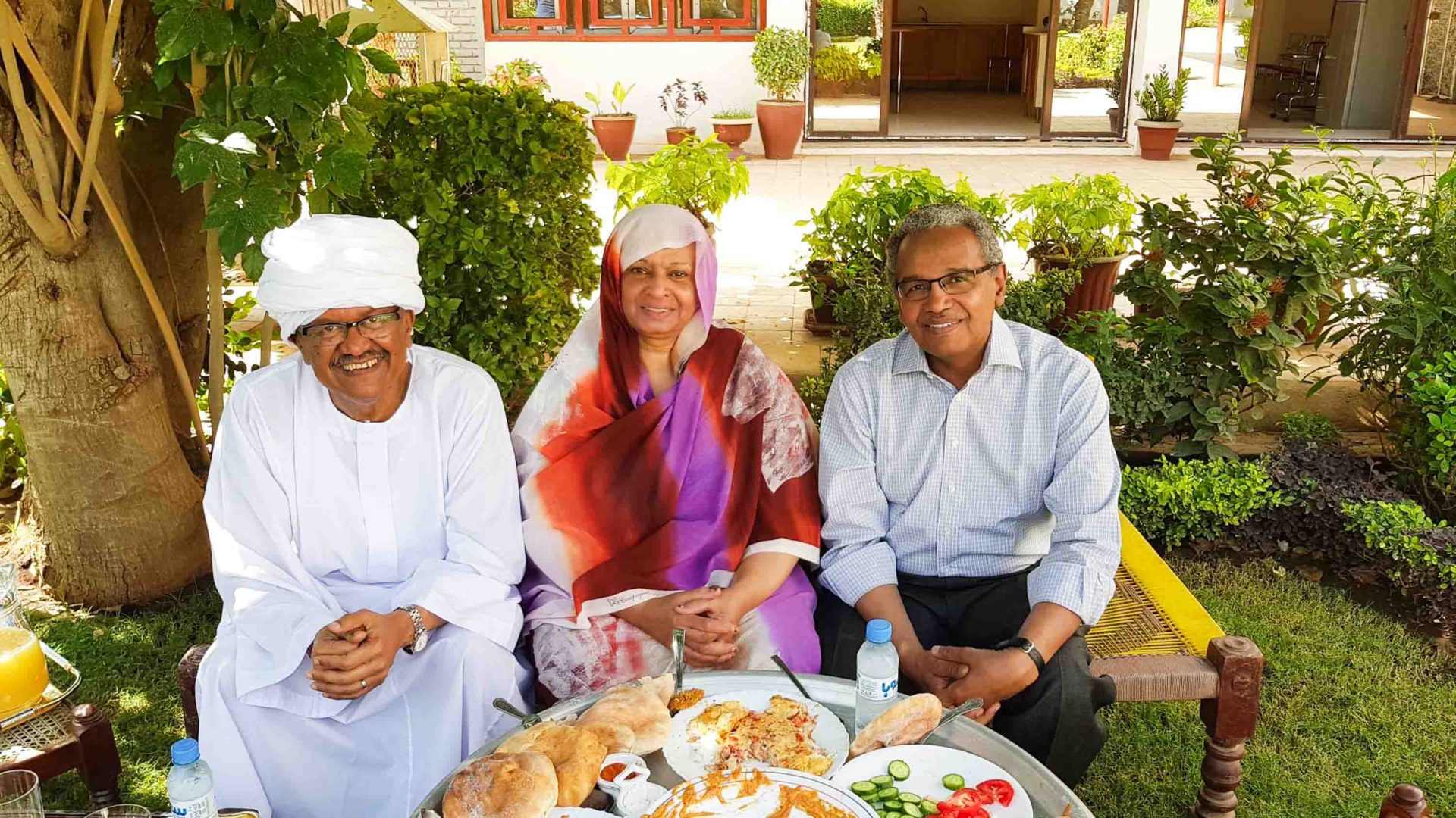Three people sit around dishes of food.