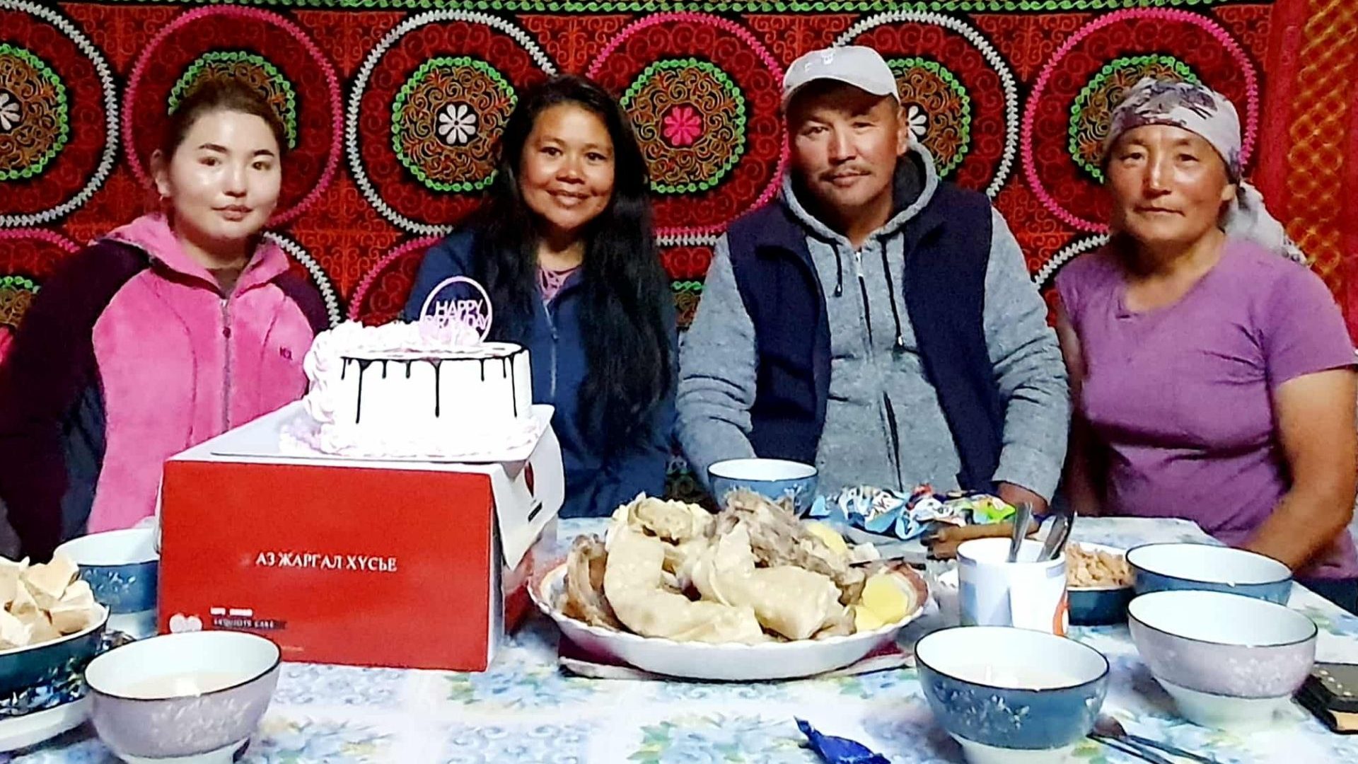 A photo of a homestay host, her parents and the founder of the homestay tour operator sat at a dining table full of food.