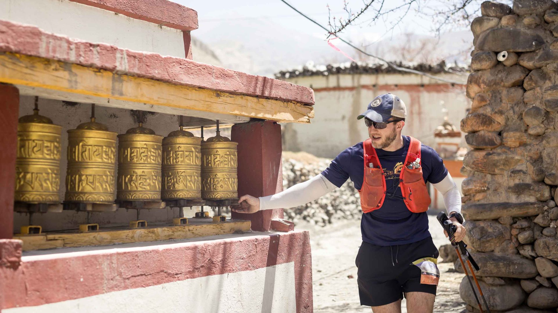 A man in hiking gear turns some prayer wheels.