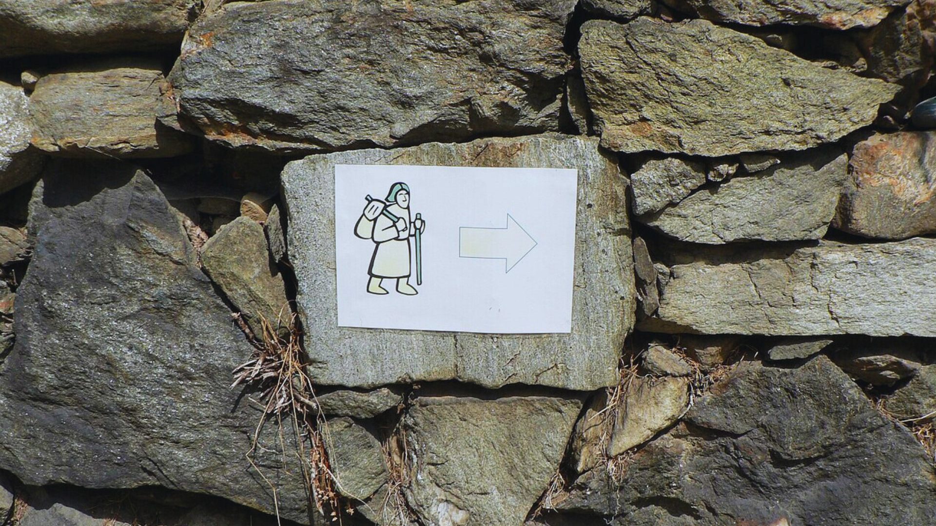 Rock wall with plastic sign of pilgrim walking and arrow directing right