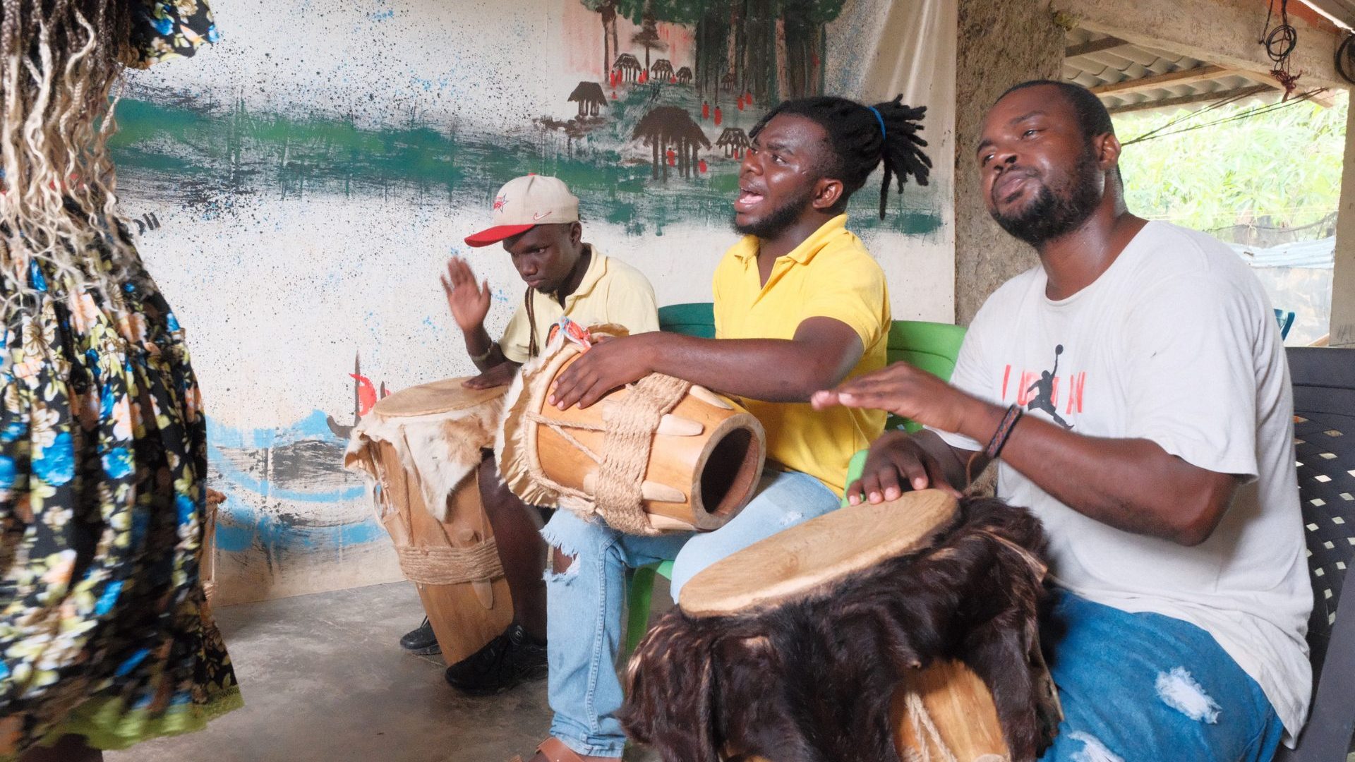 Three men smile and play hand drums.