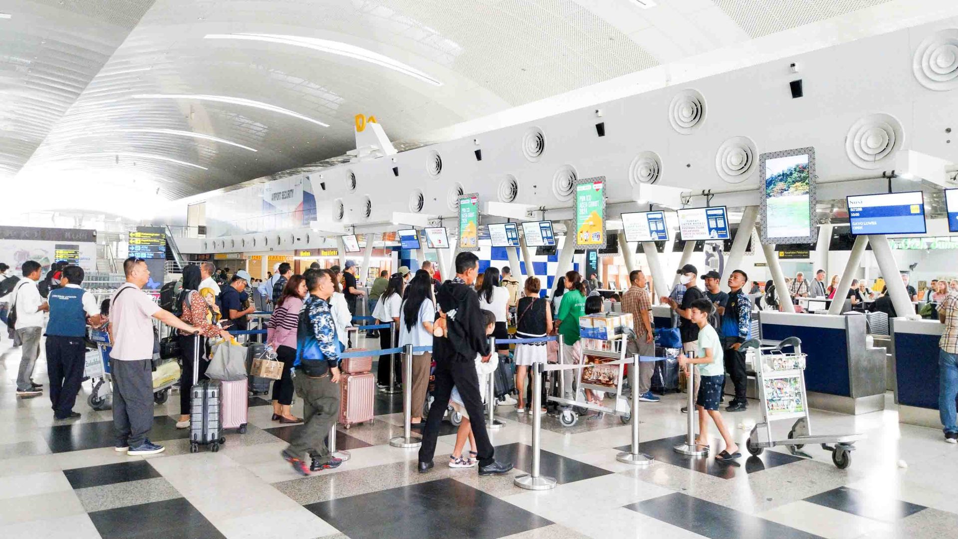 Queues of people with luggage wait to check in at an airport.