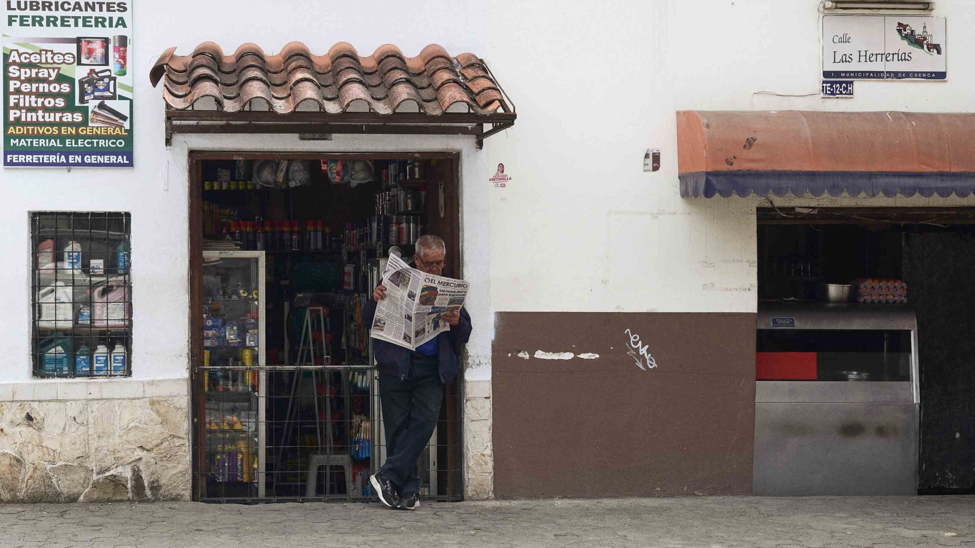 A man stands in a doorway and reads a newspaper.