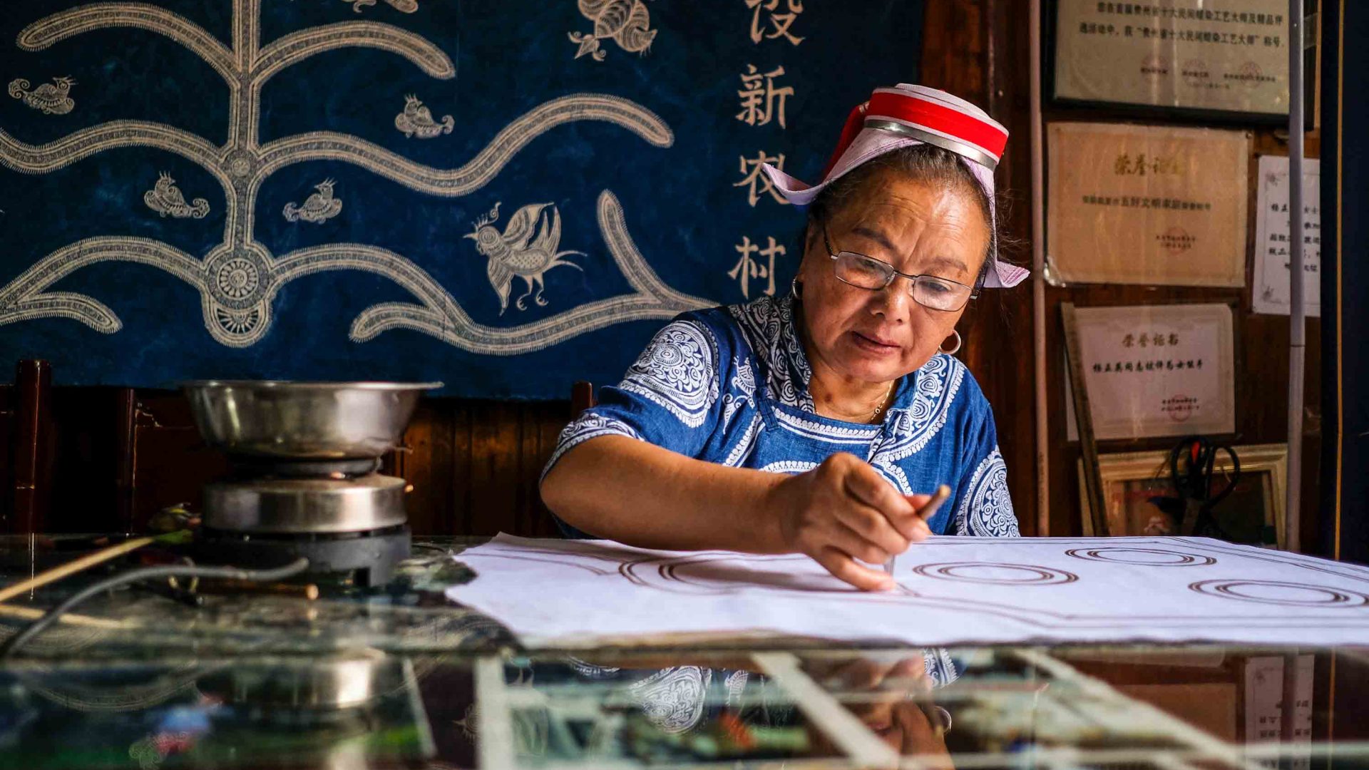 A woman works on her batik at a table.
